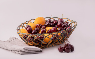 The fruits of the cherries and apricots in a wicker basket on a white background.