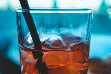 Close up of a tall glass of italian Spritz, famous cocktail with sparkling wine an orange flavored liqueur. Sky and beach on the background, beautiful color contrasts.