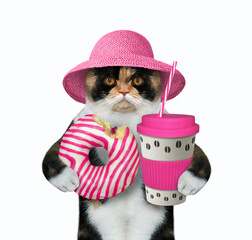 The multicolored cat in a straw hat is holding a pink striped bitten donut and a paper cup of...