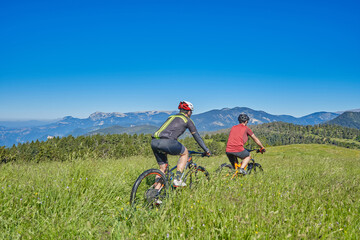 Fototapeta premium two men on mountain bike in a green field with blue sky