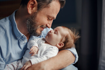 Closeup portrait of middle age bearded Caucasian father hugging and kissing newborn baby. Male man parent holding child. Authentic lifestyle touching tender moments. Single dad family life concept.