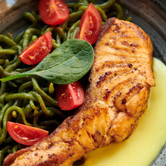 Salmon steak with green pici pasta, cherry tomatoes and cheese sauce. Healthy dish with red fish in the restaurant. Square photo closeup. Mediterranean cuisine.