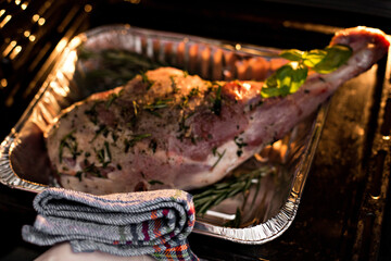 Meat steak baked in foil with fresh herbs and vegetables.  Woman's hand gets out of the oven. 
oven-cooked meat