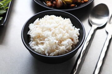 Thai jasmine rice in the black dish with spoon and fork on the grey table