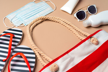 Beach bag with beach items and protective mask on beige background. Coronavirus summer concept
