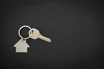 Silver key house with house shaped keychain on black leather background. 