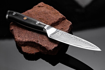 A large kitchen knife with a black handle on a dark background. Knife with a wide sharp blade....