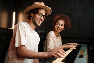 Young stylish musicians happily playing on piano keyboard recording song in modern recording studio