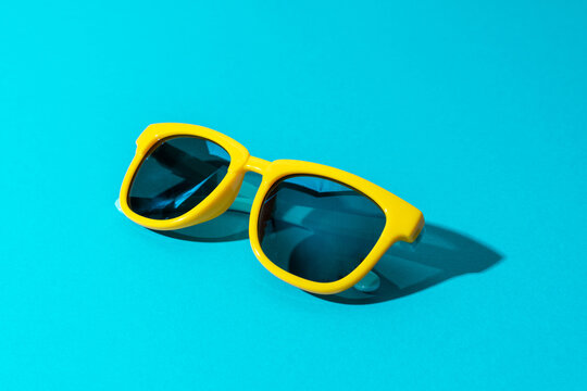 Close-up image of plastic sunglasses on turquoise blue background in perspective. Minimalist photo of stylish yellow sunglasses with harsh shadow as summer concept.