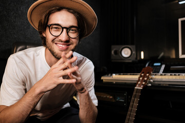 Portrait of handsome cheerful music producer happily looking in camera creating music in recording...