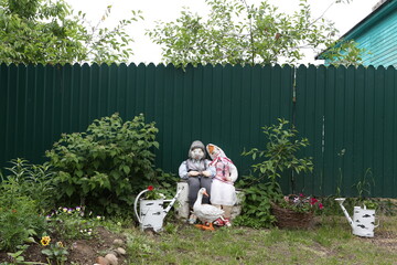 Vintage wooden rural house in Suzdal town, Russia. Folk style in gardening. Summer garden with flowers. Home decor. Decorative dolls as old russian people: woman and man. Family