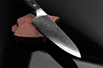A large kitchen knife with a black handle on a dark background. Knife with a wide sharp blade....