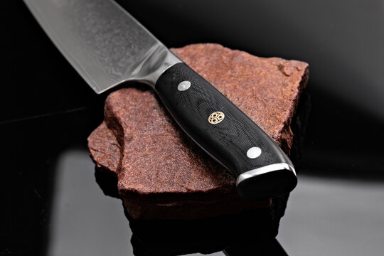 A large kitchen knife with a black handle on a dark background. Knife with a wide sharp blade. Scratched steel surface of the knife blade. 