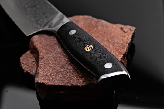 A large kitchen knife with a black handle on a dark background. Knife with a wide sharp blade. Scratched steel surface of the knife blade. 