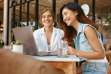 Women Chatting Online At Cafe. Girls In Casual Clothes Using Laptop For Video Meeting. Comfortable Digital Nomad Lifestyle With Modern Technologies For Communication.