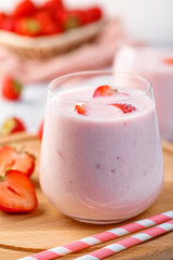 Glass with strawberry smoothie or milkshake on wooden table. Summer drink.