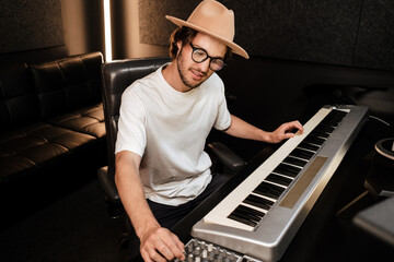 Young musician composing new song on midi piano in sound recording studio. Attractive guy playing on electric piano in studio