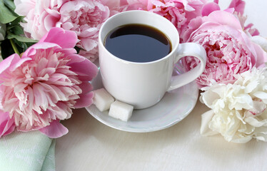 Peonies and coffee. White mug with black coffee on a background of delicate peony flowers. Close-up, no people. Light background. There is room for text.