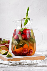 Detox water with fruits, berries and mint in glass pitcher on the white wooden table. Healthy nutrition drink
