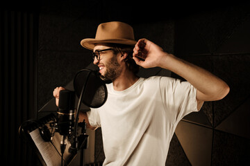 Handsome stylish musician happily dancing and singing while recording new song in modern studio