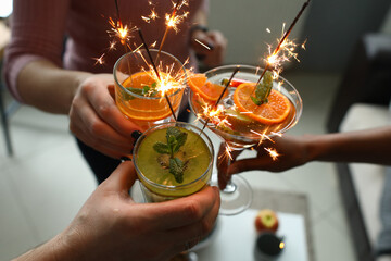 Goup of people holds cocktails in their hands with sparklers. Party and celebration concept