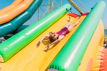 Happy little girl rides a water inflatable slide in a water Park, summer Sunny day, entertainment,...