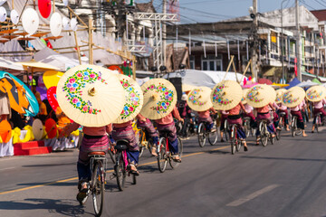 Group of women in traditional costume hold umbrella and ride bicycle parade show  at Bosang umbrella festival Chiang Mai, Thailand.