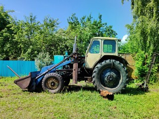 old rural tractor near fence and green trees on a sunny day