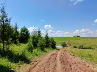 Fototapeta na wymiar winding road in a field near green trees and a small lake on a sunny day