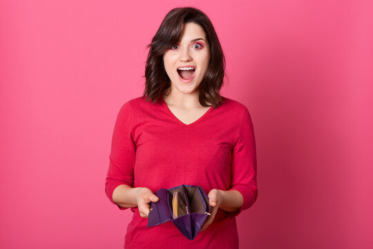 Happy surprised woman holding wallet full of money, win big sum of money, standing with widely opened mouth and excited facial expression, lady wearing red shirt.