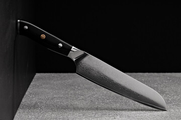 A large kitchen knife with a black handle on a dark background. Knife with a wide sharp blade. Scratched steel surface of the knife blade. 