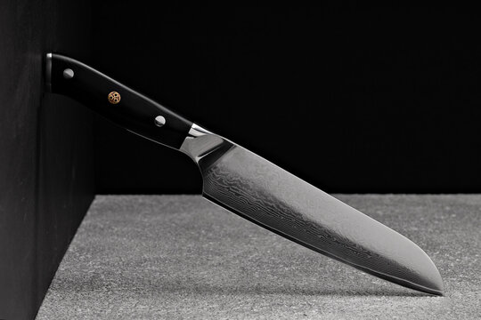 A large kitchen knife with a black handle on a dark background. Knife with a wide sharp blade. Scratched steel surface of the knife blade. 