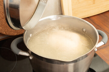 A healthy wholesome chicken breast broth is cooked on a stove in a saucepan