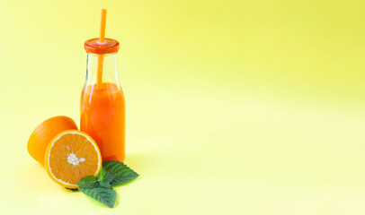 Minimalistic composition. Bright, juicy image. Fresh citrus juice with mint in a glass bottle with a tube. Yellow background. Empty space for text