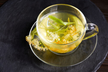 Transparent glass cup of tea with linden on a dark background. Top view