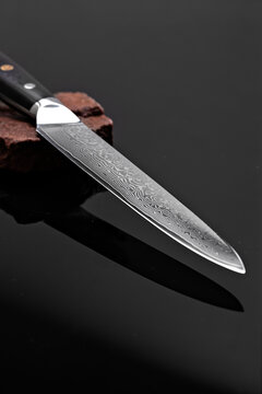 A large kitchen knife with a black handle on a dark background. Knife with a wide sharp blade. Scratched steel surface of the knife blade. 