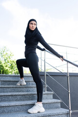 young muslim sportswoman in hijab standing on stairs outside
