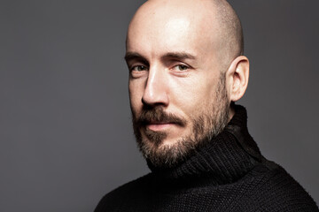 Fashion Portrait of a 40-year-old man standing over a light gray background in a black sweater....