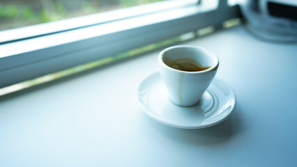 white cup and plate fill with coffee espresso on white table beside window light cool tone stock photo