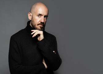 Fashion Portrait of a 40-year-old man standing over a light gray background in a black sweater. Close up. Classic style. Bald shaved head. Copy-space. Studio shot