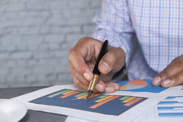 close up of man hand with pen analyzing bar chart on paper 