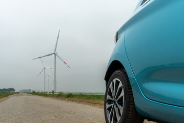 Fototapeta na wymiar Blue electric car in front of a wind turbine on a dirt road