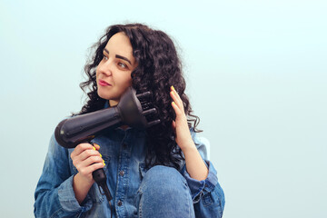 Woman using a modern hairdryer at home. Woman makes herself curly hairstyle. Beauty and haircare concept. - obrazy, fototapety, plakaty