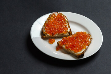 Two slices of bread with butter and red caviar on a white plate.