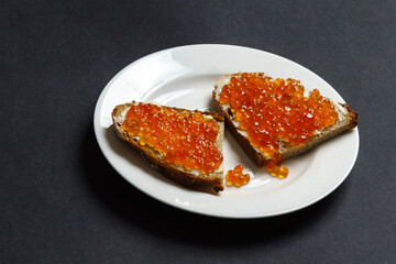 Slices of bread with butter and red caviar on a white plate.