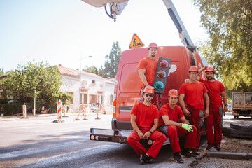 Five construction caucasian workers in red work suits stand next to a crane van on the construction...