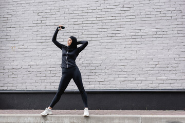 muslim woman holding smartphone with blank screen near brick wall