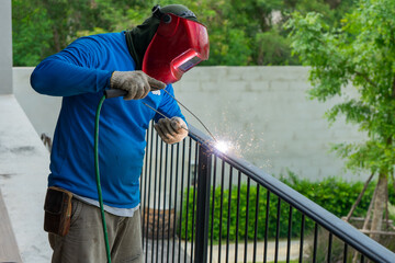 Closeup portrait of welder with mask welding the steelwork of black fence with sparking light and...