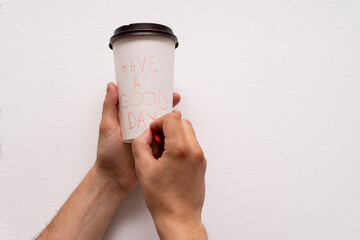 Caucasian male hands writing message with have a good time at paper togo takeaway coffee cup with black cover at white background.