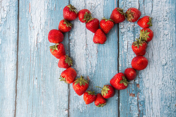 Fresh ripe perfect strawberry laid out in the heart on blue wooden background. Fresh strawberry as texture background. Natural food backdrop with red berries. Strawberries sale in food shop.